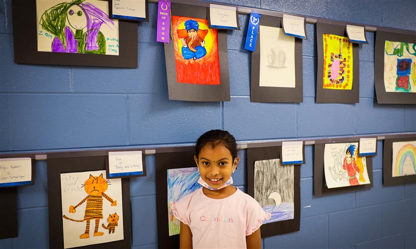 A girl wearing a pink shirt stands beneath student artwork